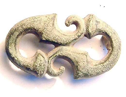 A small green copper-alloy openwork belt plate: a pair of mirrored S-scrolls with curled terminals.